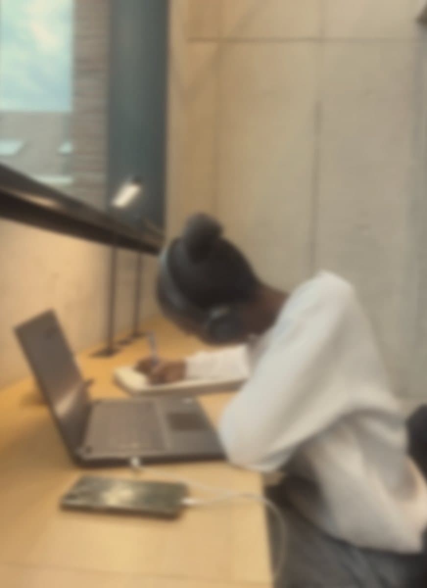 A student in headphones writing in a notebook beside a laptop